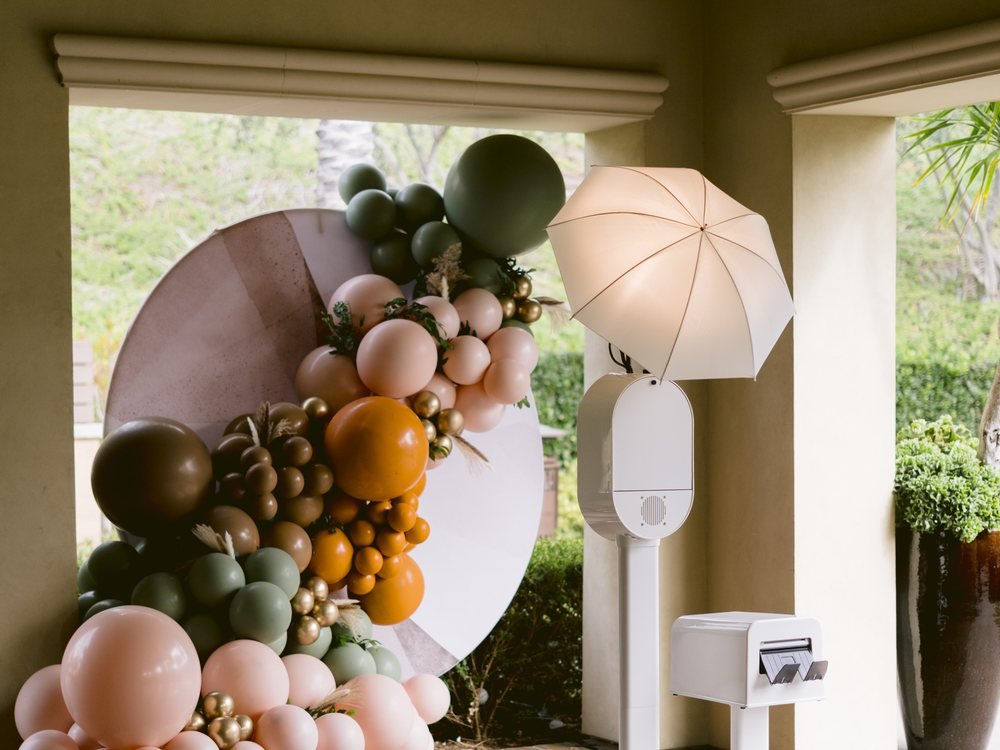 The open-air booth, umbrella flash, and printer set up beside a balloon arch