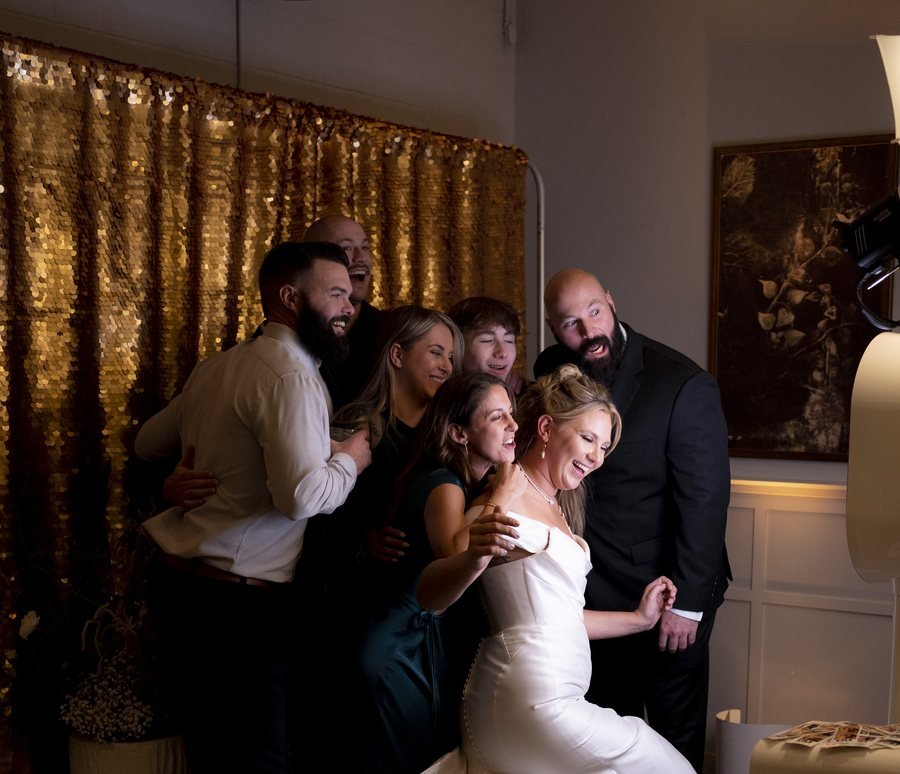 A wedding party laughing together at the booth in front of a gold backdrop